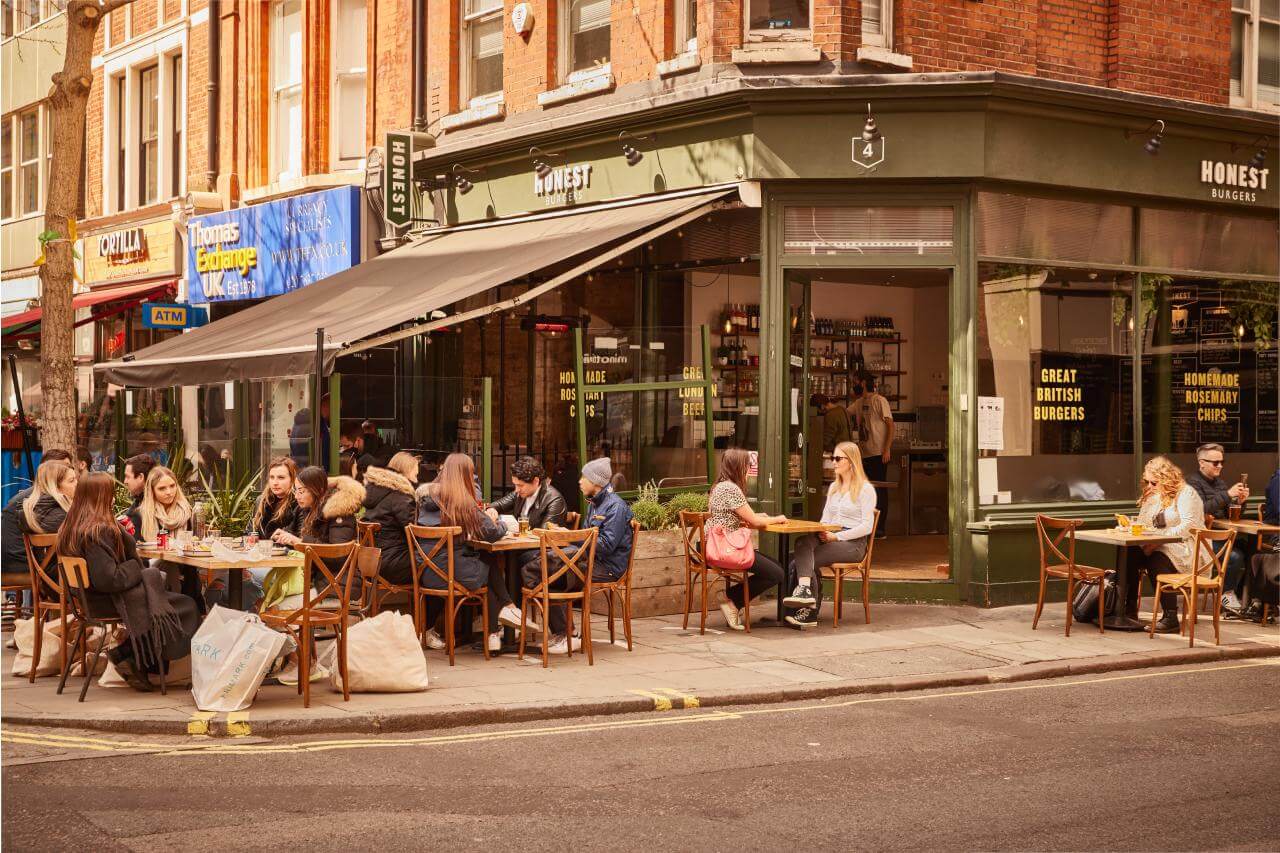 People enjoying a meal outside of an Honest Burgers restaurant on sunny day.